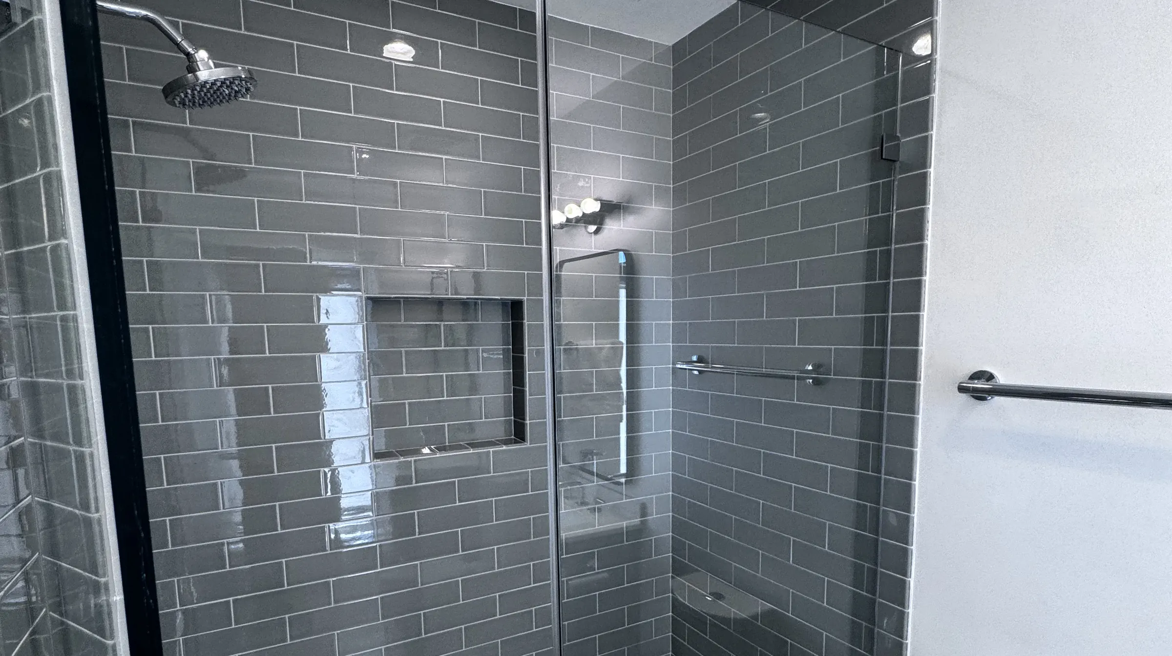 Glass-enclosed walk-in shower finished in grey subway tile with a recessed niche