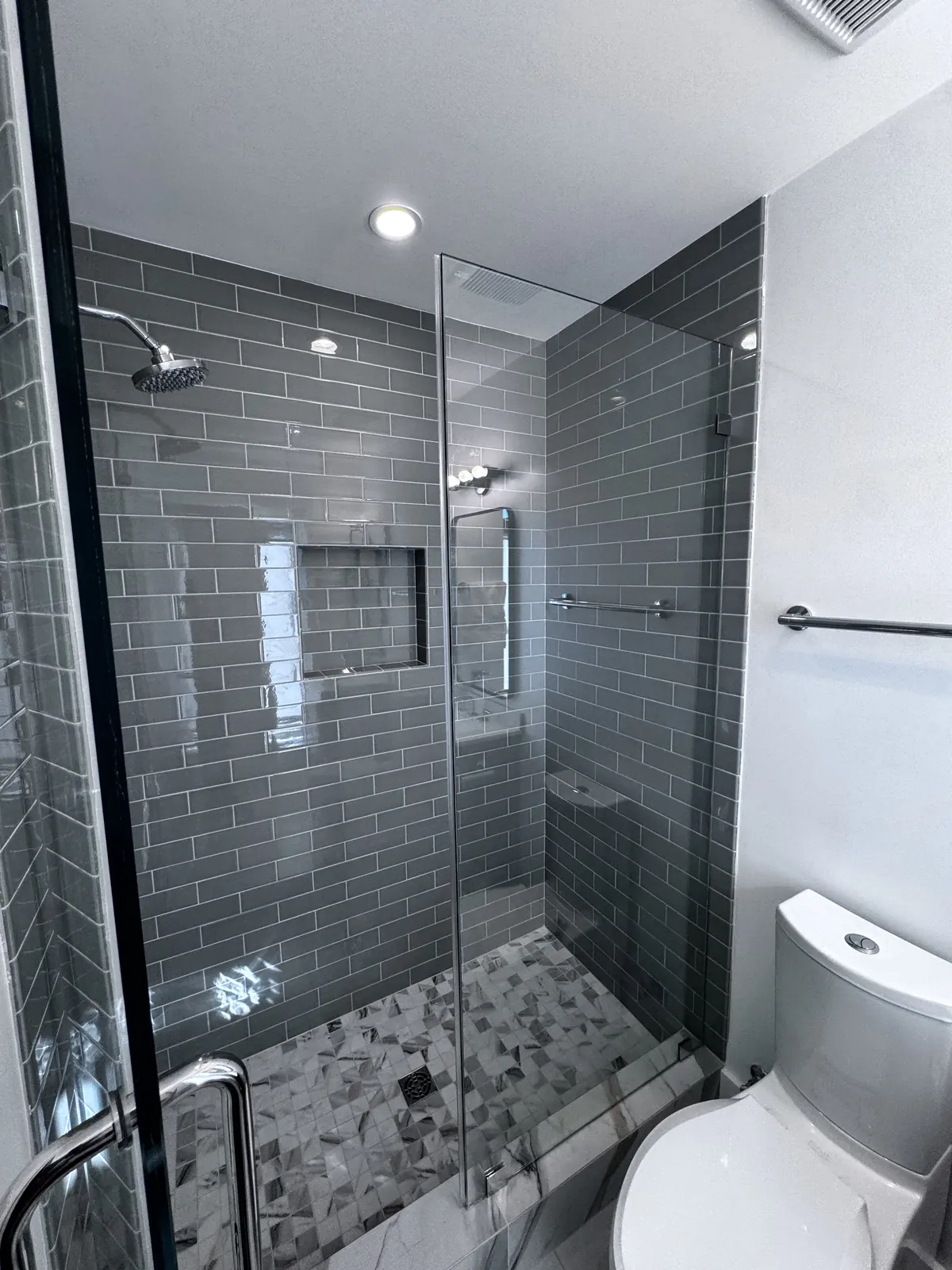 Completed walk-in shower with grey subway tile and a frameless glass enclosure