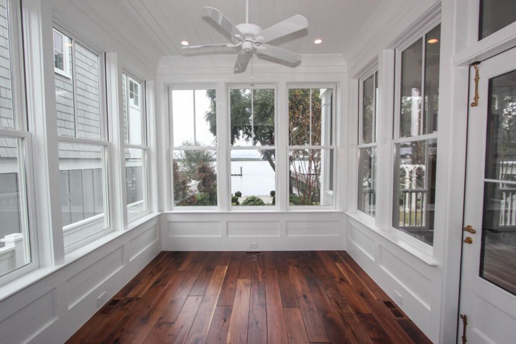 Empty sunroom with large windows overlooking water and greenery