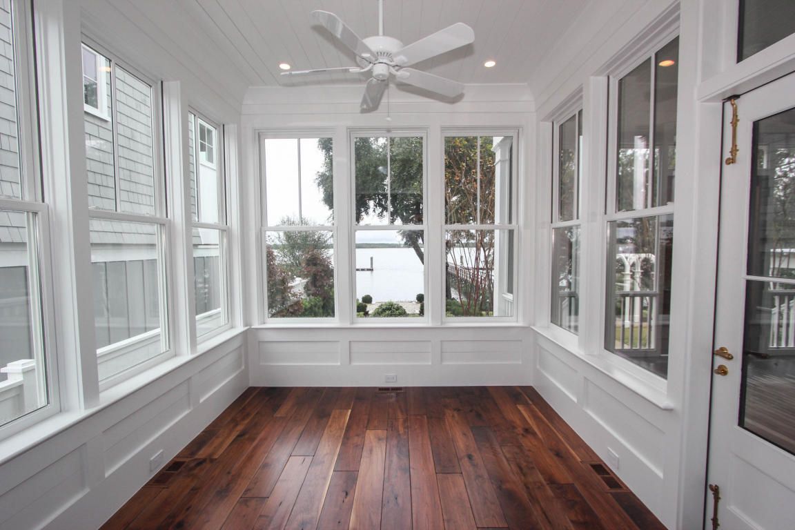 Empty sunroom with large windows overlooking water and greenery